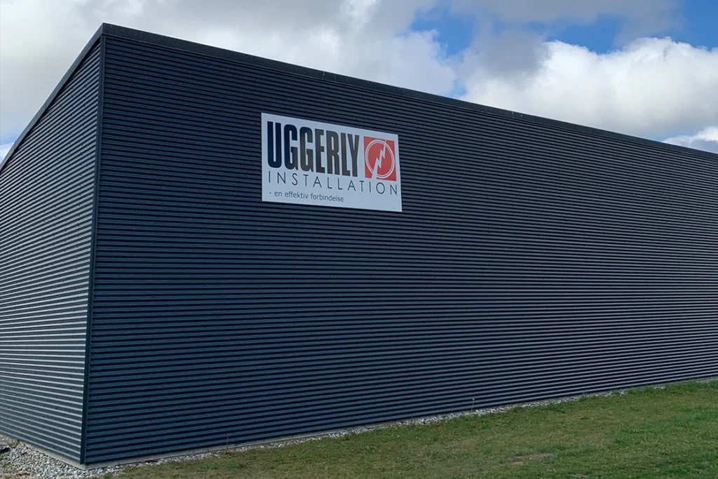 Fronten af Uggerly Installations elektrikerafdeling i Odense. En sort bygning med et stort firmaskilt. 