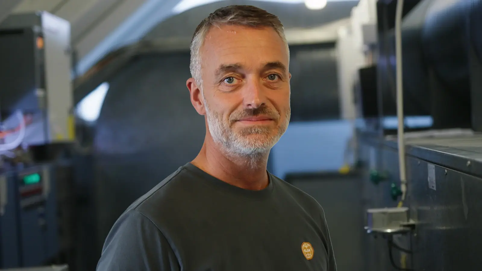 Elektriker Esbjerg står i et teknikrum og kigger mod kameraet 